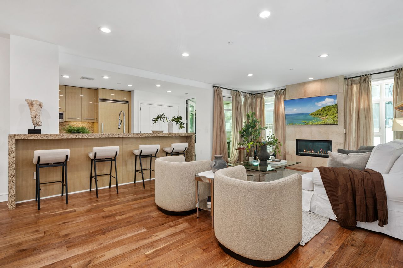 Elegantly staged living room featuring walnut hardwood floors, a limestone fireplace, and a seamless transition into a luxury kitchen with Viking appliances.