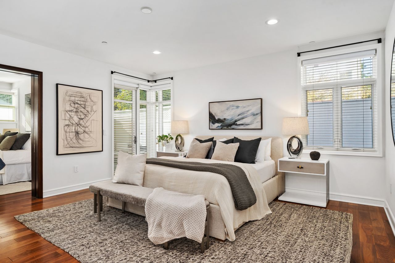 Professionally staged primary suite in a Beverly Hills luxury condo featuring walnut hardwood floors, contemporary artwork, a plush king bed, and corner glass door access to a private terrace.
