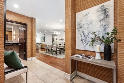 Elegantly styled formal entry foyer featuring stone tile flooring, grasscloth wallpaper texture, contemporary abstract art, and a glimpse into the open-concept living and dining area.
