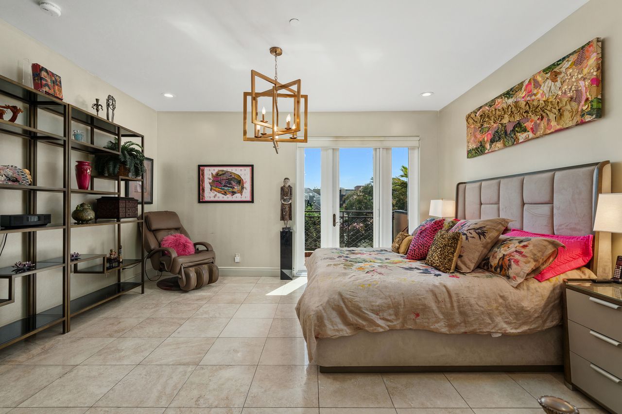 Spacious primary bedroom suite with geometric chandelier and French door balcony access at 137 S Spalding Dr #401 Beverly Hills