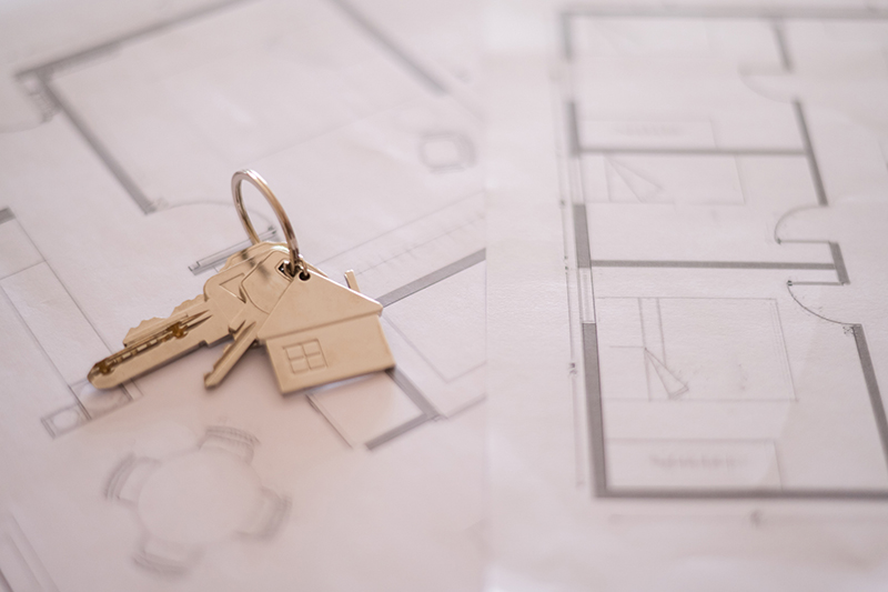 House shaped keychain with keys is lying on architectural plans, representing the concept of buying, selling, renting, or building a new home