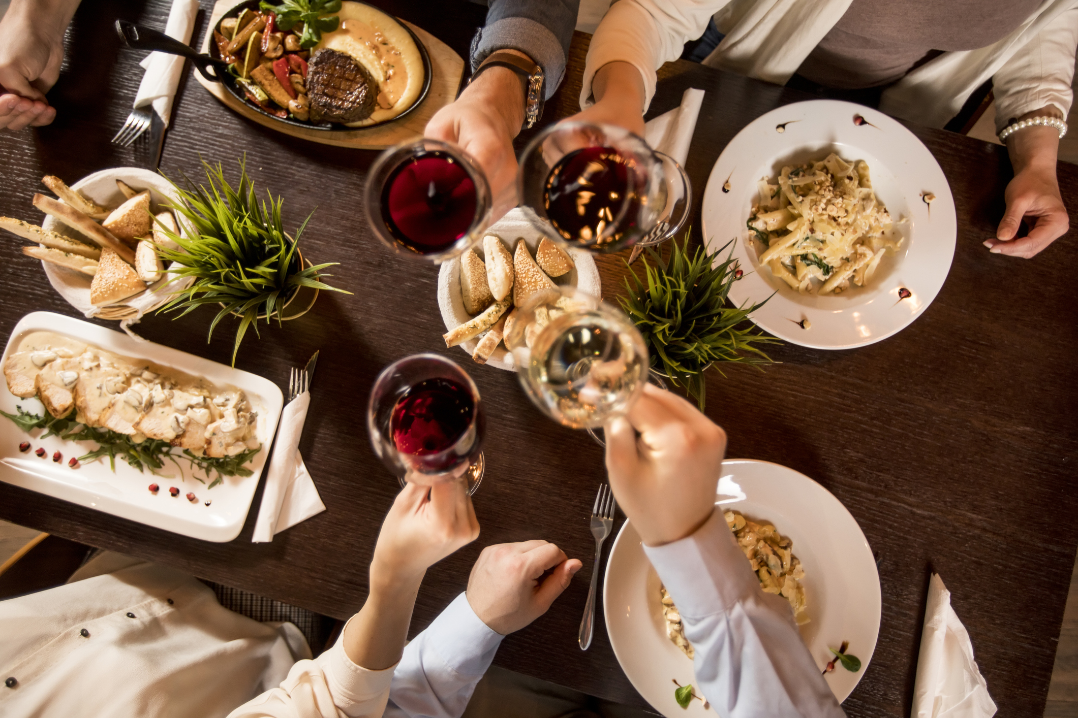 Four hands with red wine toasting over served table with food in the restaurant