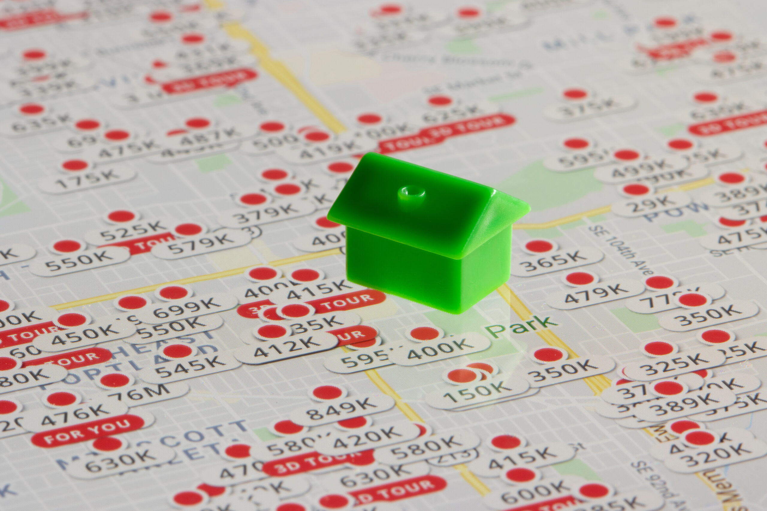 Portland, OR, USA - Nov 30, 2021: A green plastic toy house sits on top of the Zillow website's map page showing listed properties in Portland, Oregon. Housing market concept.
