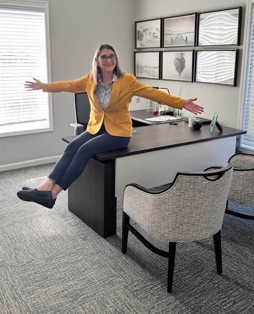 Realtor sitting on desk in office with arms open, welcoming and approachable