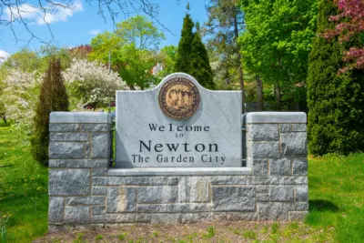 The Welcome to Newton, The Garden City stone monument with bronze city seal and spring blossoms, civic entrance for Newton Massachusetts and its 13 villages