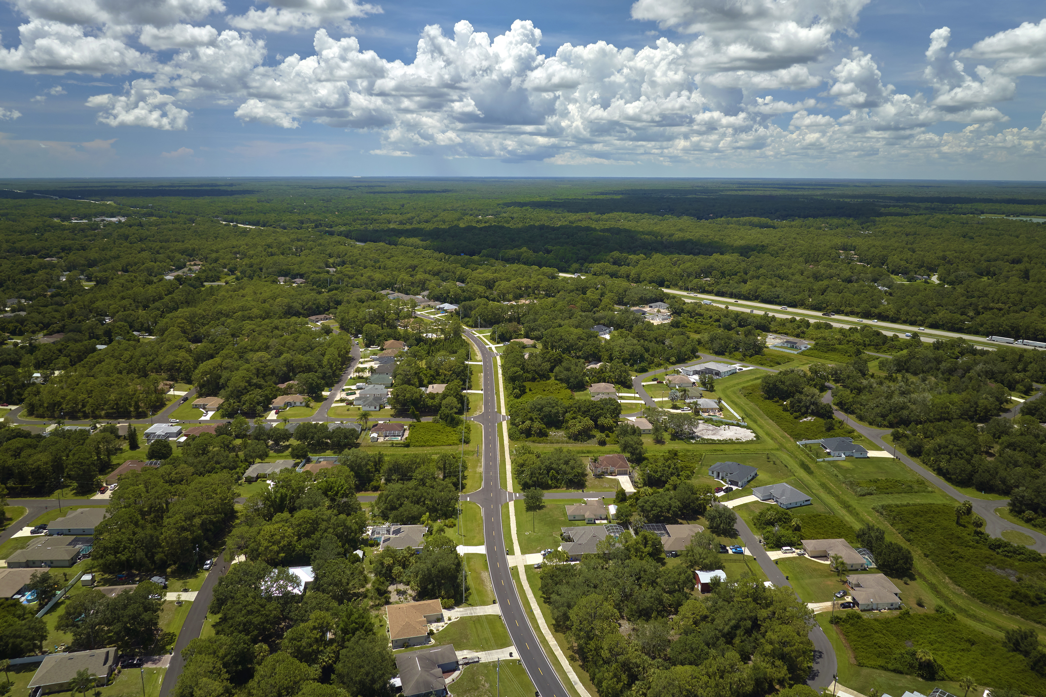 Aerial view of street traffic with driving cars in small town. American suburban landscape with private homes between green palm trees in Florida quiet residential area.