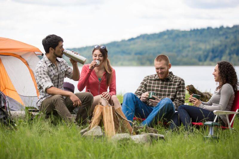 group of people camping on grass with lakeview at their back
