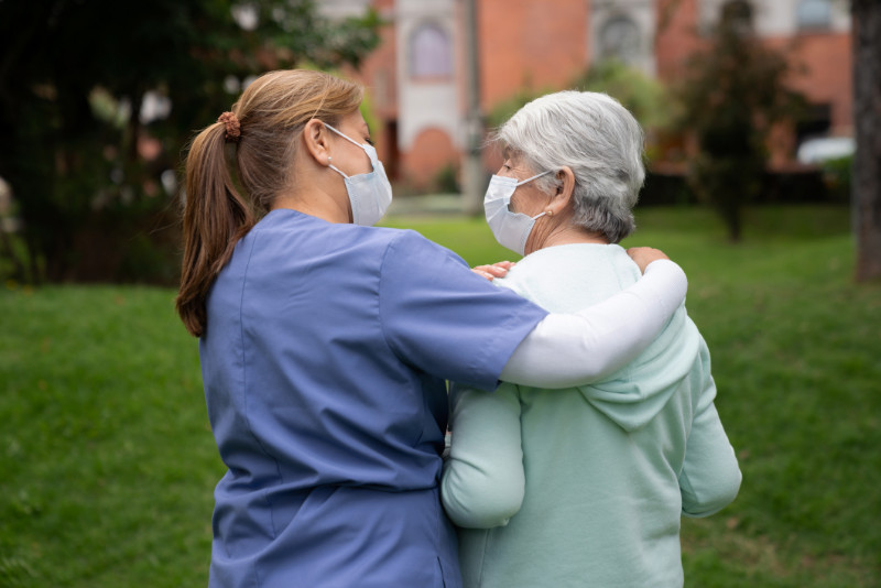 An elderly woman and her caregiver walking in a park