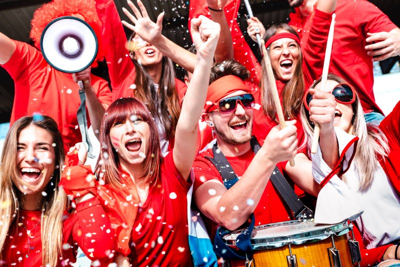 Football supporter fans cheering with confetti watching soccer match cup at stadium tribune