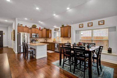 Open concept kitchen and dining area with granite countertops, stainless steel appliances, wood floors, and large windows in a San Marcos TX home.