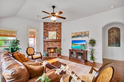 Inviting living room featuring a brick fireplace, warm wood flooring, and large windows in a San Marcos Texas home.