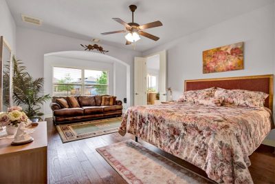 Oversized primary bedroom with sitting area, wood floors, ceiling fan, and natural light in a San Marcos TX home.