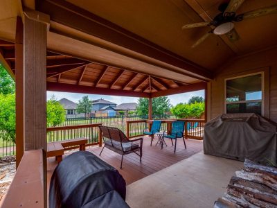 Covered back patio with wood deck, ceiling fan, seating area, and backyard view in a San Marcos TX home.