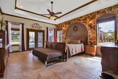 Texas Hill Country estate San Marcos TX primary bedroom with stone accent wall, wood beam ceiling, and patio access