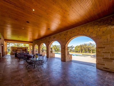 Texas Hill Country estate San Marcos TX covered outdoor patio with stone arches, seating area, and view of pool and BBQ area