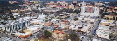 Aerial view of downtown San Marcos Texas featuring the historic Hays County Courthouse, Texas State University area, and surrounding commercial development.