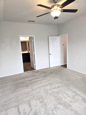 Spacious primary bedroom with neutral walls, ceiling fan, and soft carpet flooring in newer Texas home
