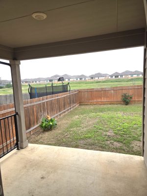 Covered back patio overlooking fenced backyard and greenbelt area behind the home