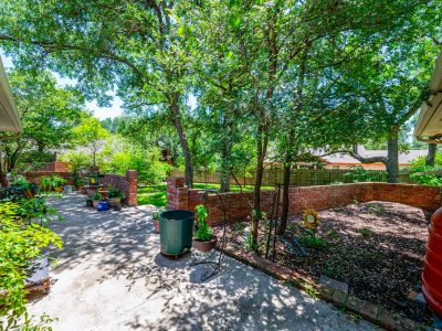Private backyard patio area with mature Cedar Elm trees and brick landscaping in San Marcos residence