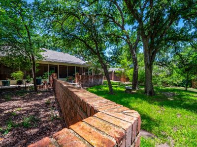 Shaded backyard with mature Cedar Elm trees and established landscaping in quiet San Marcos neighborhood