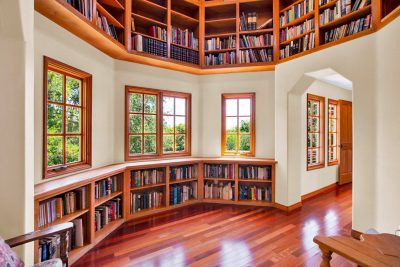 Custom library with built-in bookshelves, hardwood floors, and treetop views through oversized windows