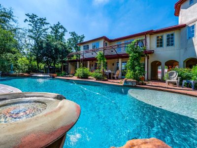 Resort-style swimming pool with tanning ledge, waterfall features, and outdoor living spaces overlooking a private natural setting