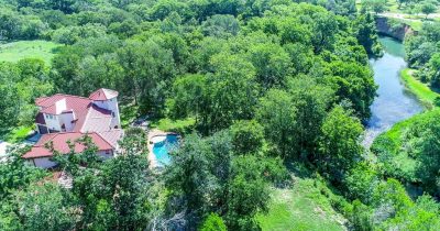 Aerial view of custom riverfront estate surrounded by mature trees with the San Marcos River flowing alongside the property