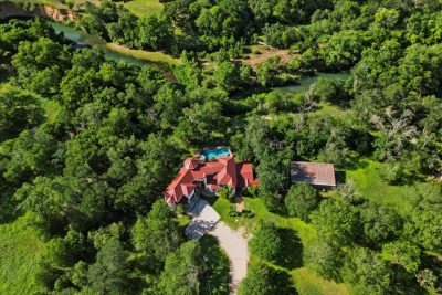 High-altitude aerial view of a custom estate nestled among mature trees with river frontage and expansive grounds