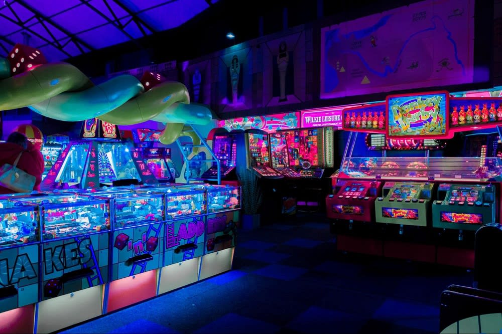 A vibrant arcade filled with colorful gaming machines and neon lights, featuring a playful green snake sculpture.