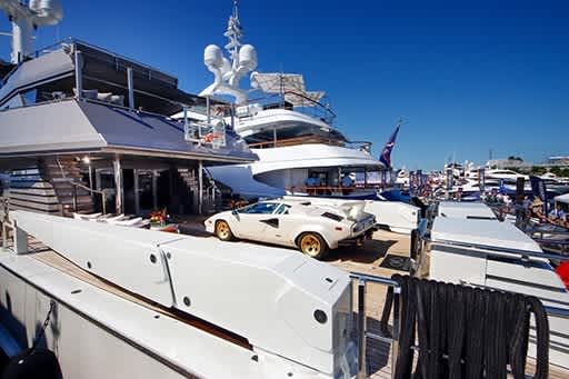 A luxury yacht with a classic car on the deck, surrounded by other boats and a clear blue sky.