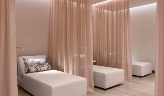 A serene spa-like room with white lounge chairs separated by soft, sheer curtains, creating a calming atmosphere.