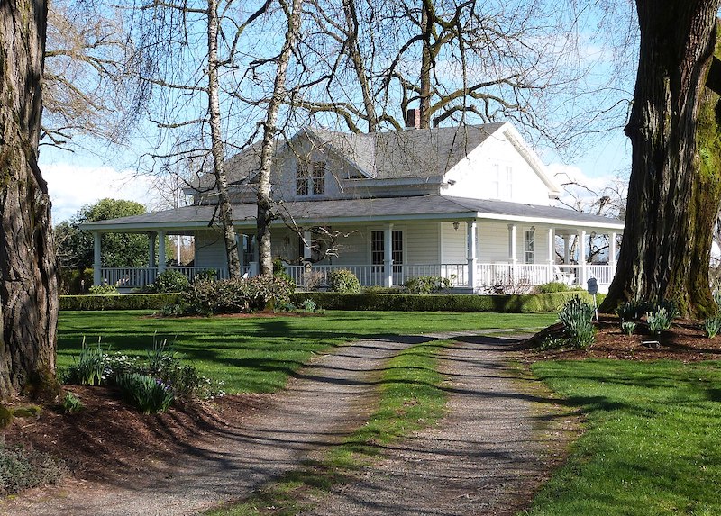 Historic farmhouse-style home with a wraparound porch and mature trees in Oregon City, Oregon.