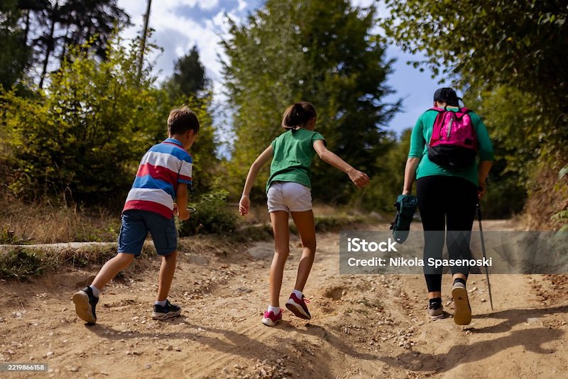Three individuals enjoy a hike through a scenic outdoor trail. The group includes two children and an adult carrying a backpack, symbolizing outdoor activity, nature exploration, and family bonding.