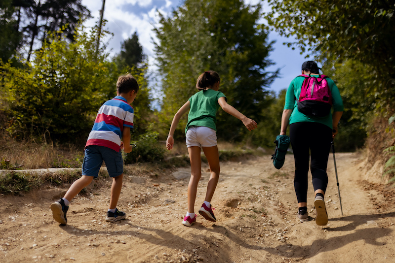 Three individuals enjoy a hike through a scenic outdoor trail. The group includes two children and an adult carrying a backpack, symbolizing outdoor activity, nature exploration, and family bonding.