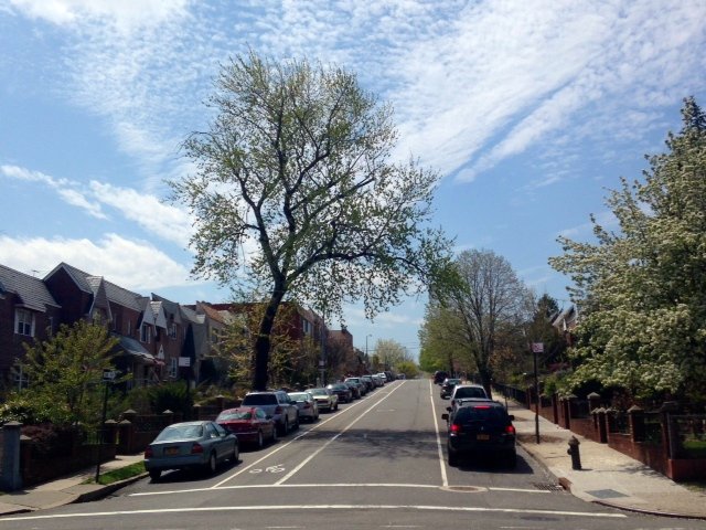 Sunlit brick rowhouses lining a residential street in Astoria, Queens under a bright blue sky — Queens NY property taxes and homeownership
