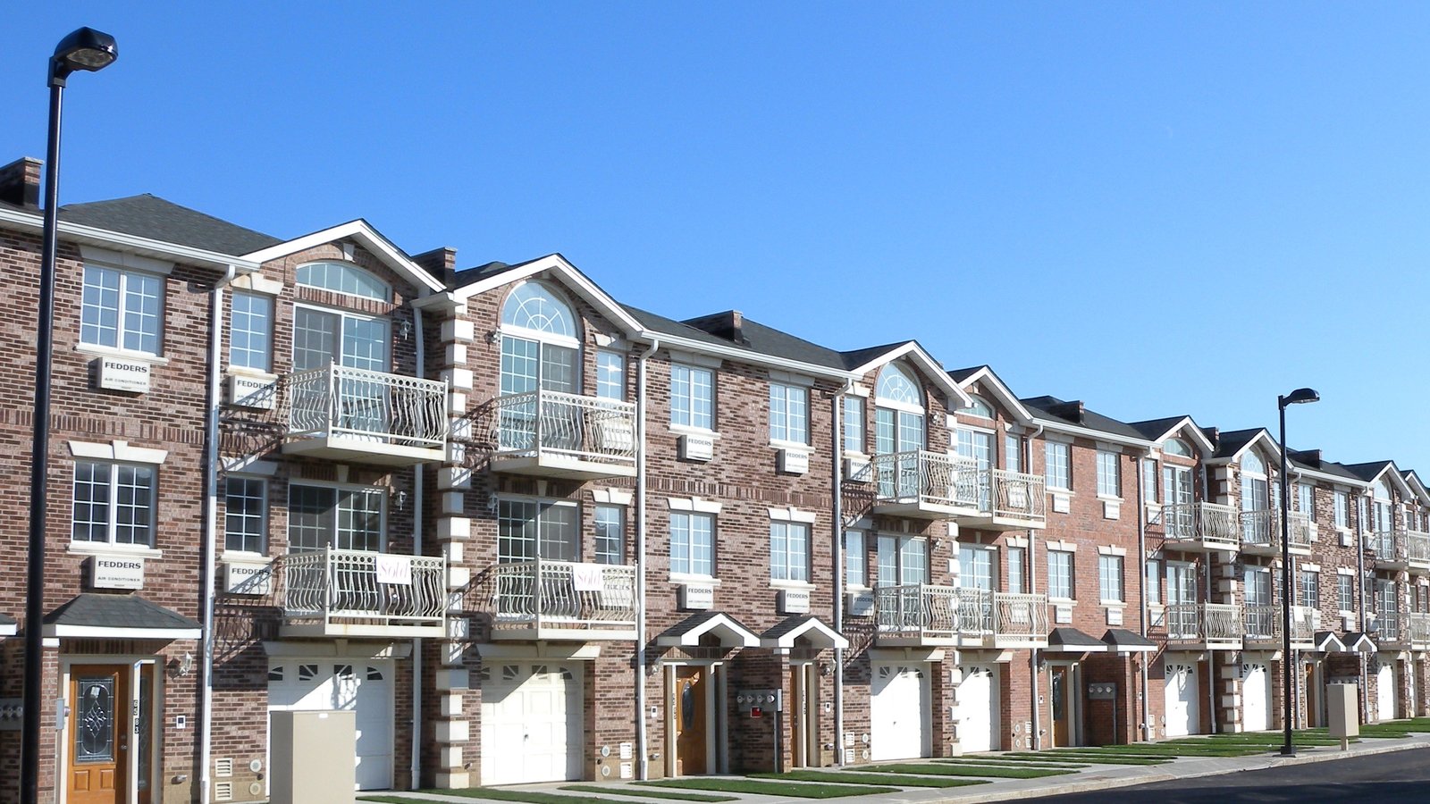 Row of newer brick townhouses with balconies and garages on a sunny day in Queens, NY — what is my home worth in Corona, Queens