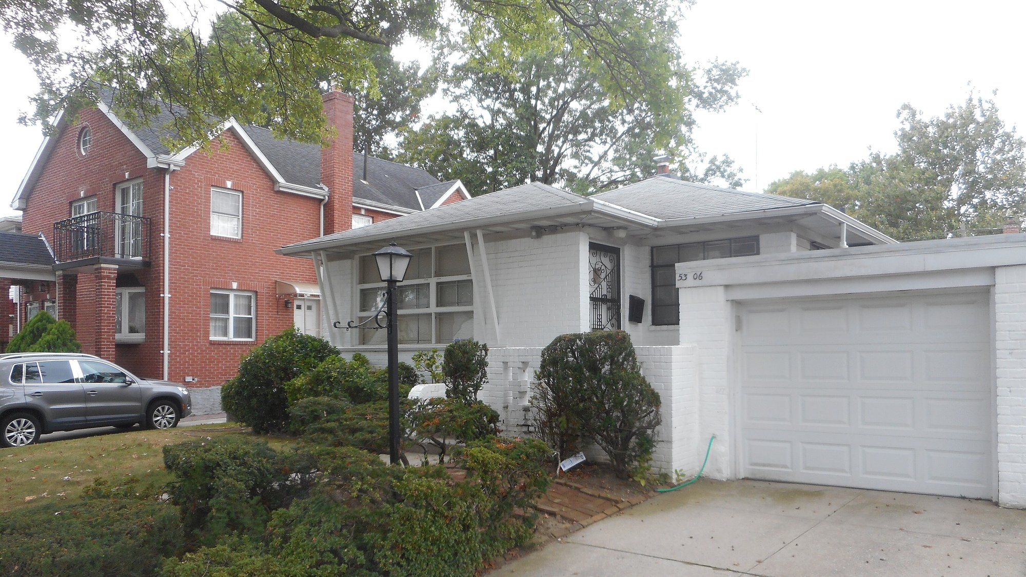 Agente de bienes raíces en Woodhaven Queens: casa de ladrillo rojo y casa moderna blanca con garaje y jardín en una calle arbolada de Bayside, Queens (foto de referencia, no es Woodhaven)