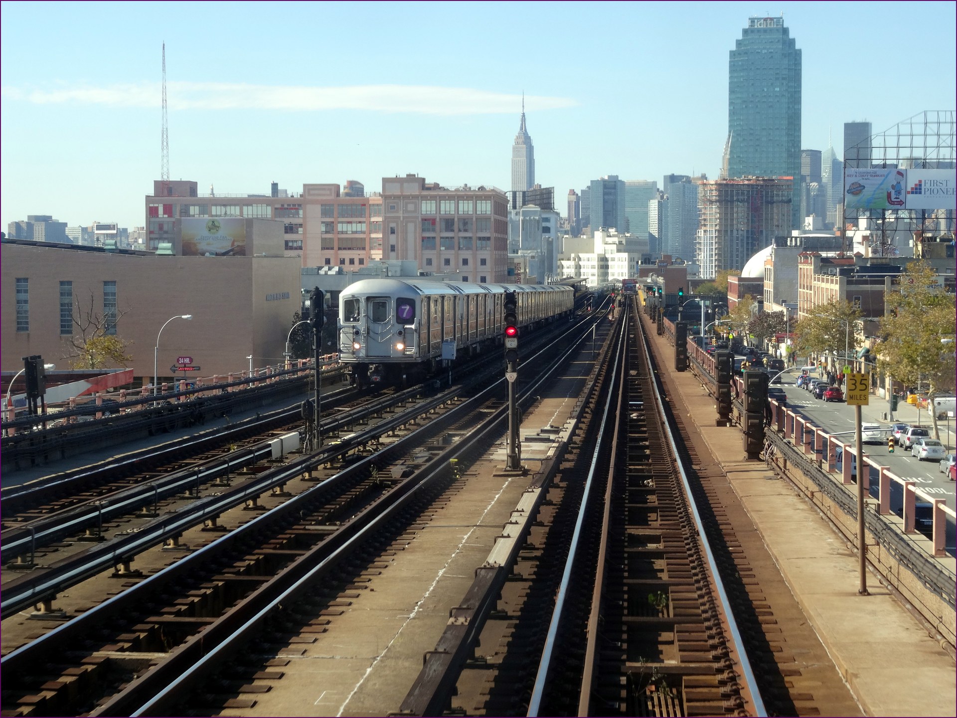 Elevated 7 subway train crossing Sunnyside, Queens, under a bright blue sunny sky