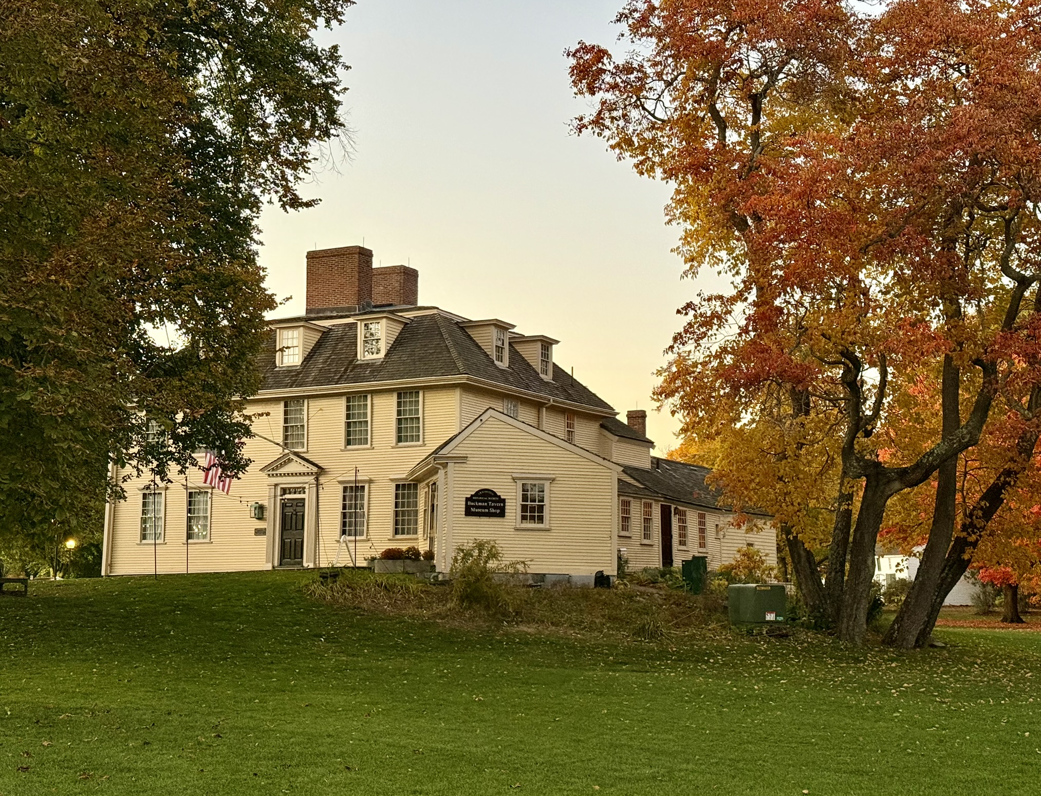 Historic Buckman Tavern in Lexington, Massachusetts, surrounded by colorful fall foliage at sunset.