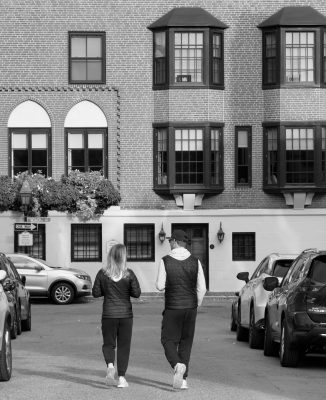 Couple walking on a Beacon Hill street in Boston with historic brick rowhouses and bay windows in the background.