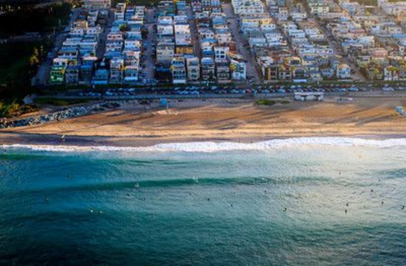 Aerial view of a beach with surfers, bordered by colorful buildings and a sandy shore.
