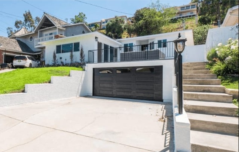 A modern house with a garage, steps leading up to a porch, and a green lawn in front. Bright, sunny day.