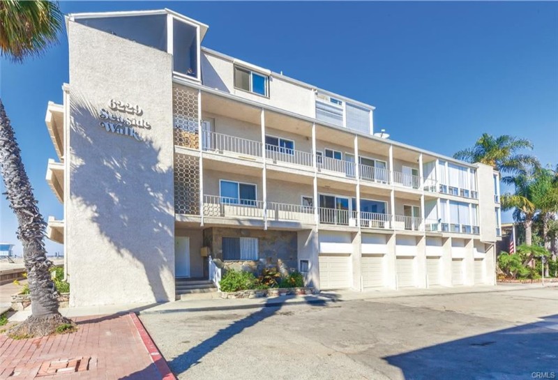 A multi-story building with balconies, labeled "Shoreside Walk," surrounded by palm trees and a clear blue sky.