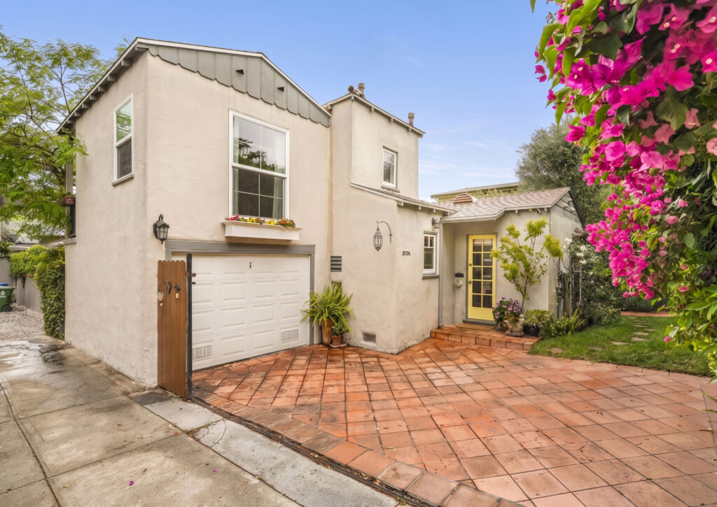 Gated single-family home exterior in Mid-City Los Angeles, featuring a driveway, yellow front door, and vibrant landscaping with bougainvillea.