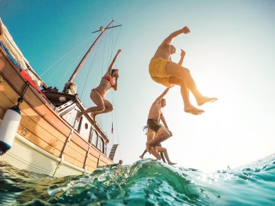 Happy friends diving from sailing boat into the sea
