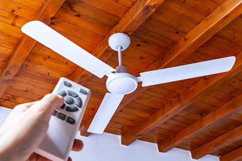 A man uses a remote control to turn on a white ceiling fan mount in austin texas