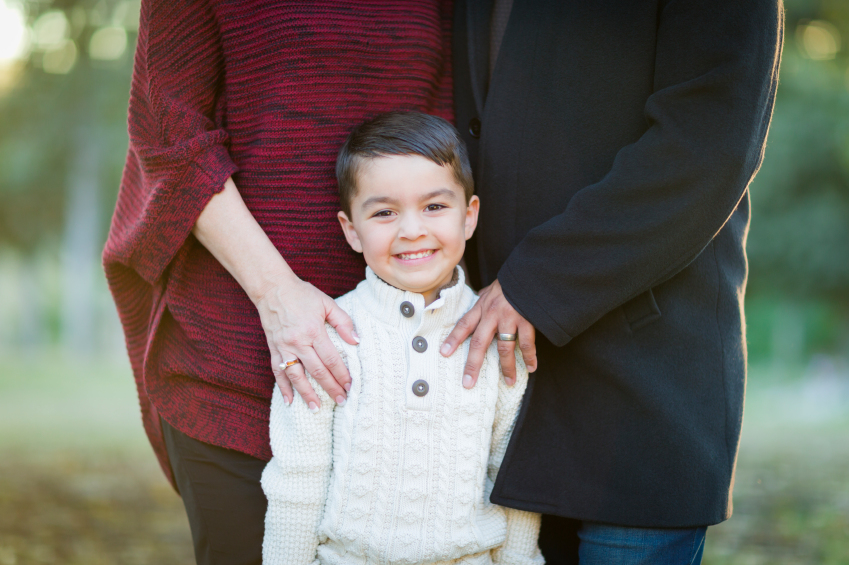 Handsome Young Mixed Race Boy Portrait Outdoors With Parents Behind.