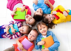 Image is six kids with books lying on the floor together. Top view.