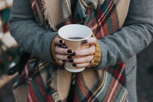 Image is of a woman holding a paper cup full of coffee.