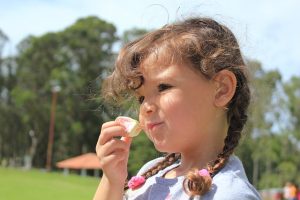 Image is of a girl at a park eating a snack.